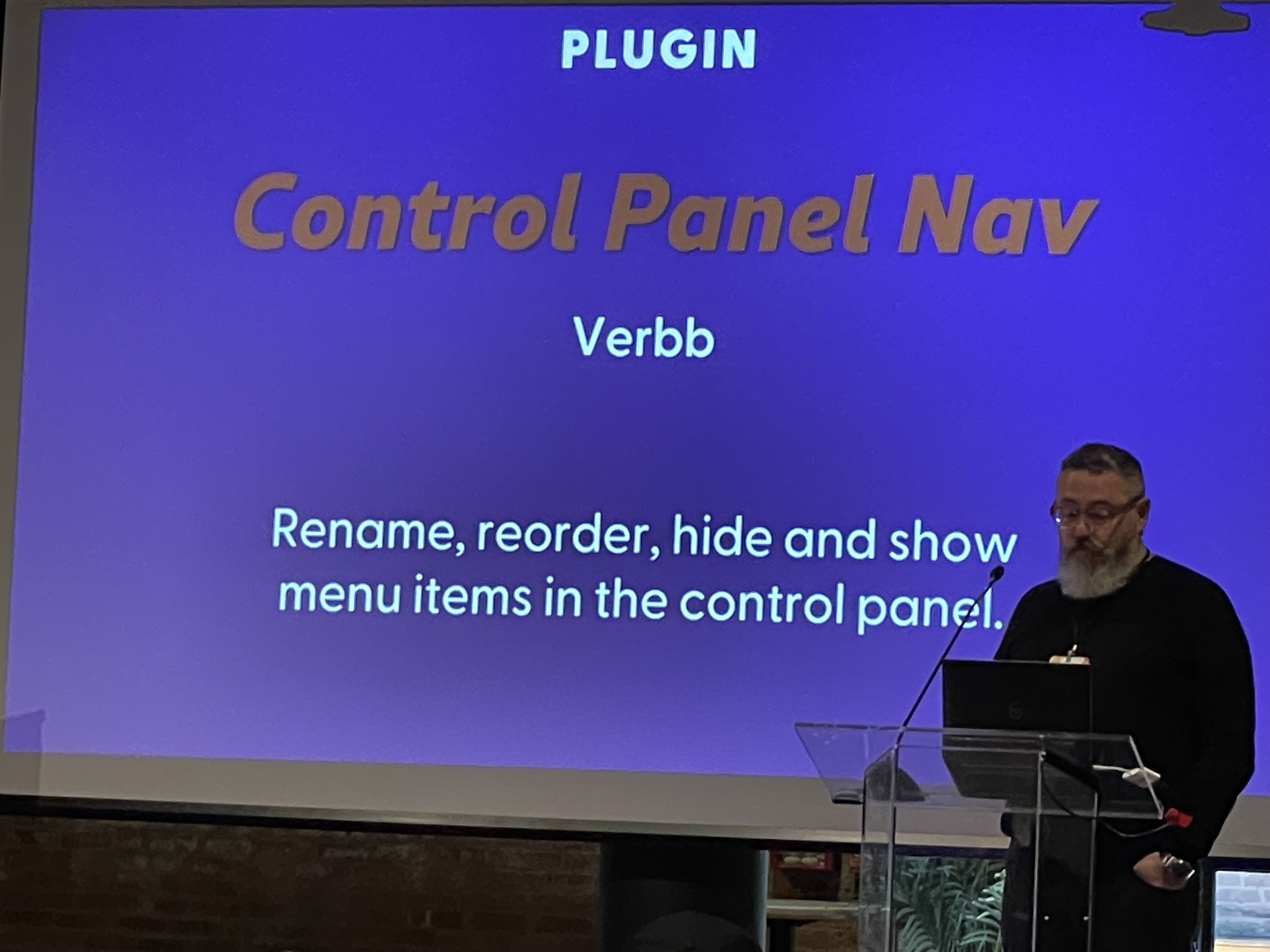 A man with a beard stands at a podium in front of a presentation slide. The slide reads "PLUGIN Control Panel Nav Verbb. Rename, reorder, hide and show menu items in the control panel.