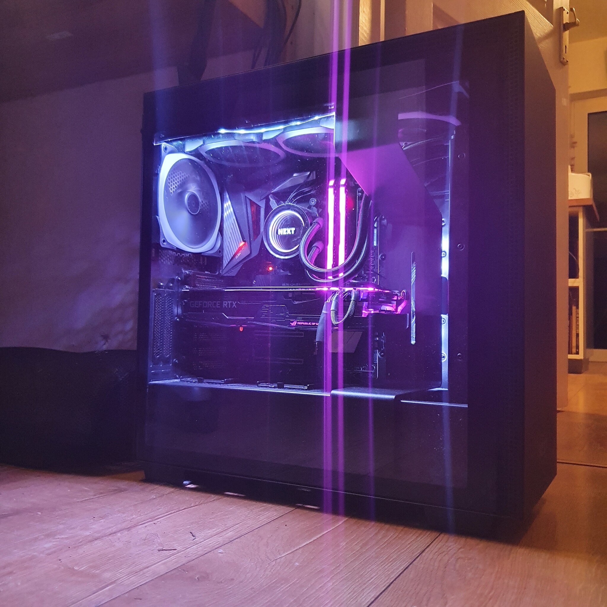 A desktop computer with a transparent side panel reveals internal components illuminated by purple and blue LED lights. The visible parts include a cooling fan, graphics card, and various cables. The computer is situated on a wooden floor.