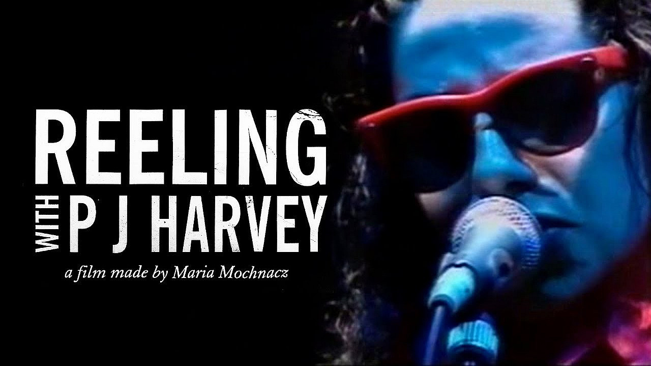 A film poster for "Reeling with P J Harvey," directed by Maria Mochnacz. It features a close-up of a person wearing red sunglasses and singing into a microphone under a blue light. The film's title and director's name are displayed in bold, white text on the left.