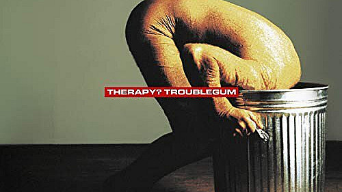 Album cover for "Troublegum" by Therapy?. It depicts a person with a shaved head and bare torso, crouching and bent forward with their head inside a large metal trash can, set against a plain background. The band and album name are in red text at the center.