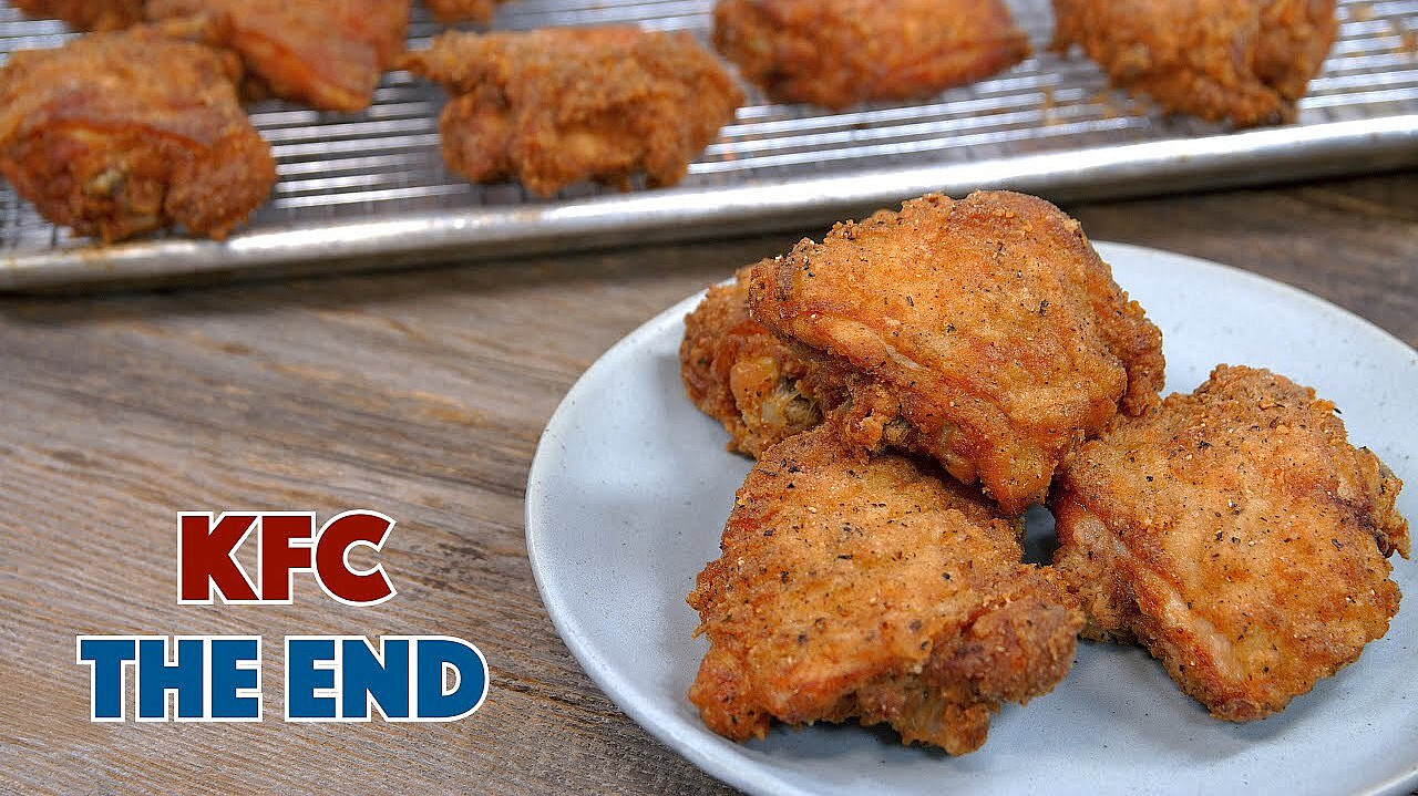 A plate with three pieces of fried chicken is placed on a wooden table. In the background, more pieces of fried chicken are on a wire rack on a baking sheet. The words "KFC THE END" are prominently displayed in the lower left corner.