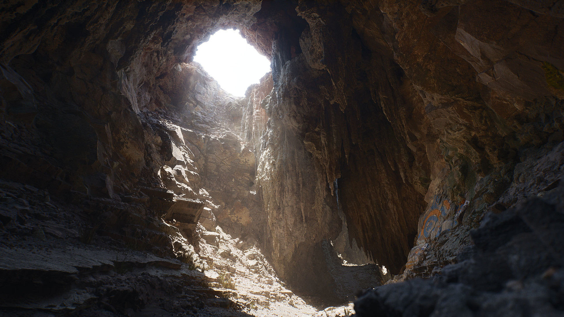 A large cave with rough, rocky walls and a wide opening at the top allowing sunlight to illuminate the cave's interior. The cave floor is uneven, with various rock formations and some colorful graffiti visible on the right wall.